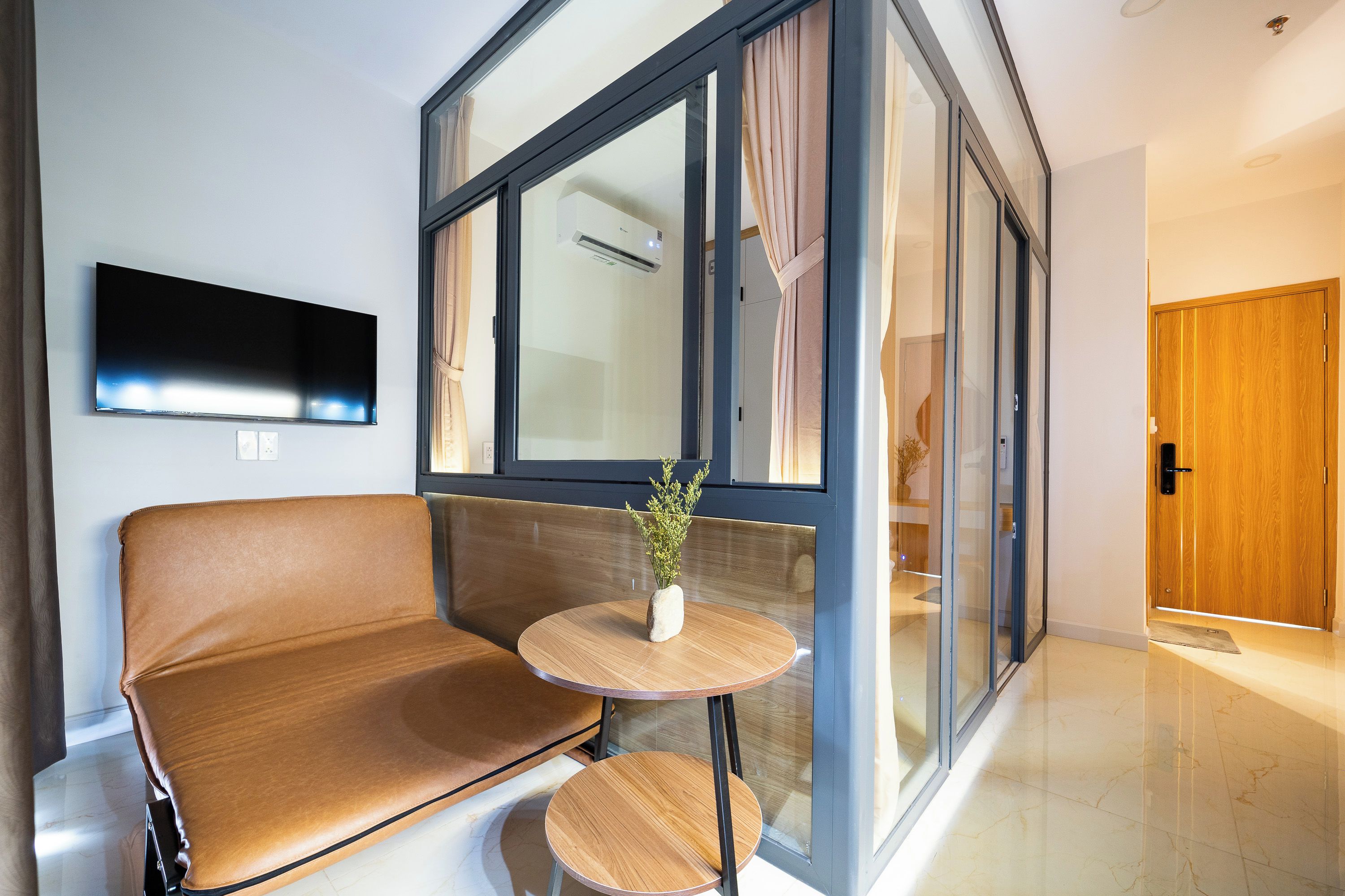 Een moderne woonkamer met een bank, een klein rond tafeltje en een flatscreen televisie aan de wand.