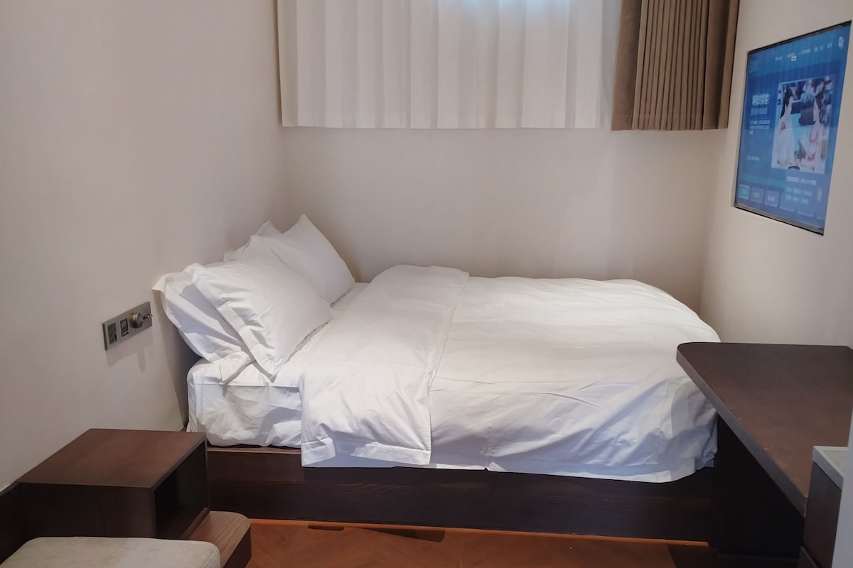 A compact room with a bed, bedside tables, and a small seating area.