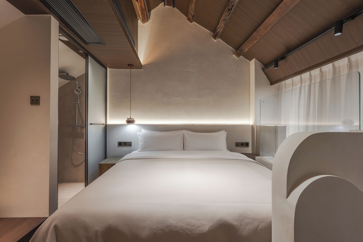 A modern bedroom with a large bed, a glass shower enclosure, and a wooden ceiling.