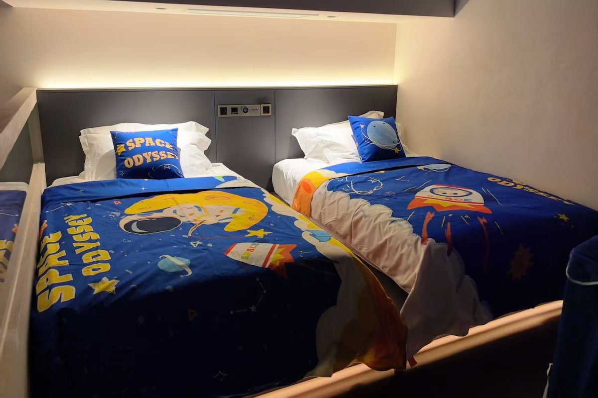 A room with two beds, each with a space-themed bedspread and pillows.