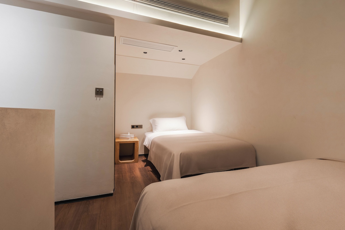 A hotel room with a bed, bedside table, and a small wooden stool.