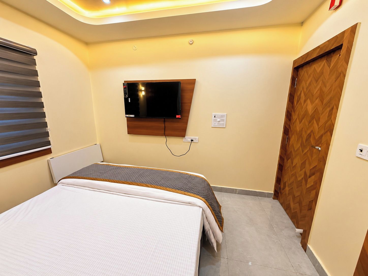Una habitación de hotel con una cama, un televisor montado en la pared y una puerta de madera.
