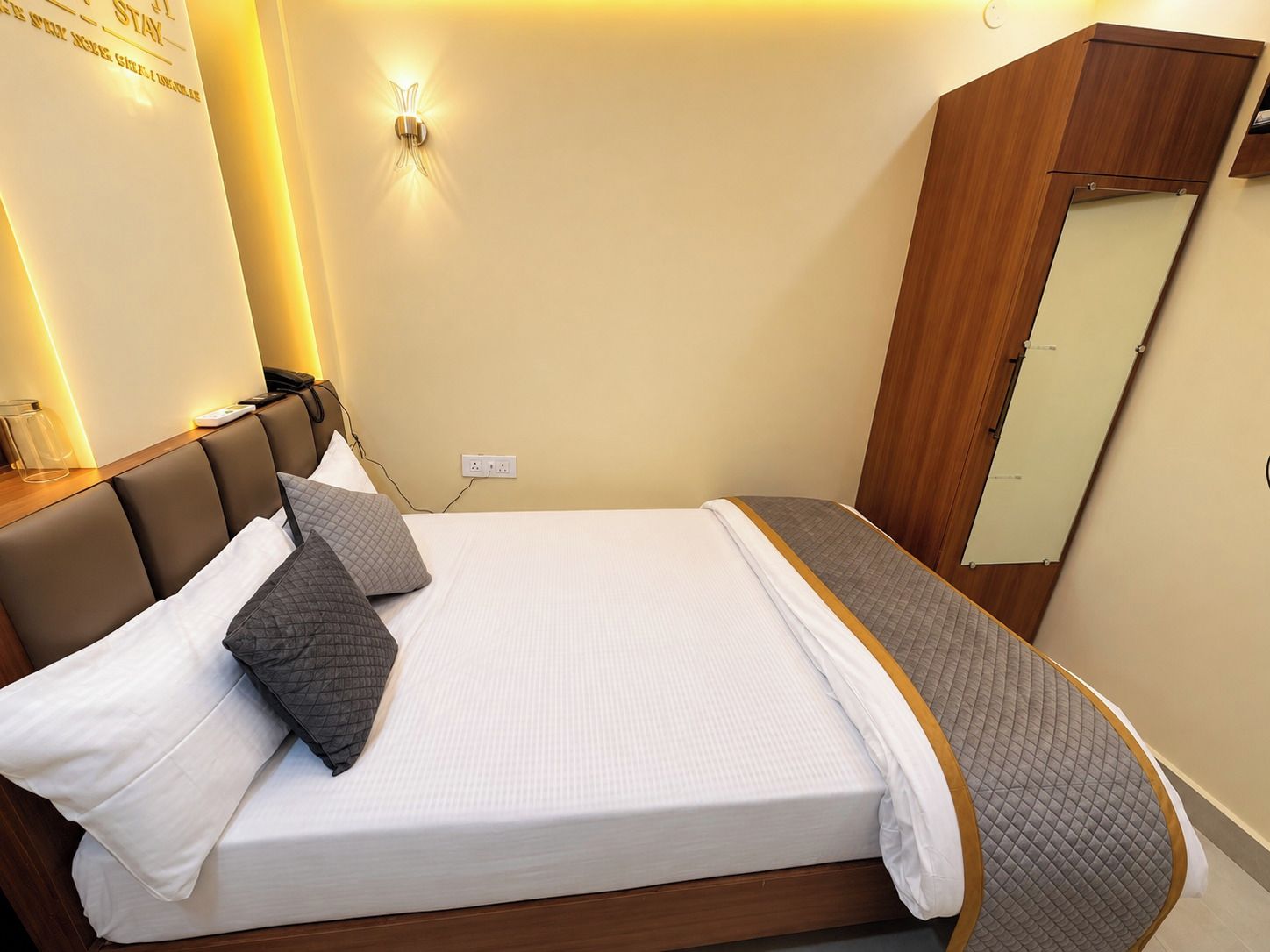 A neatly made bed with a headboard, a bedside table with a lamp, and a wardrobe.