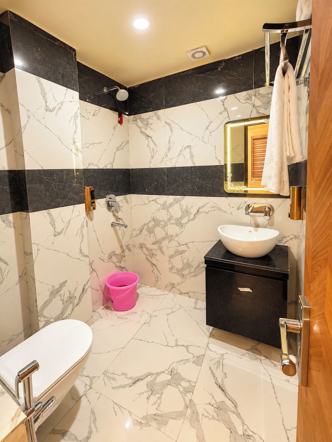 A bathroom with a white toilet, a sink with a black countertop, a mirror with a gold frame, and a shower area.