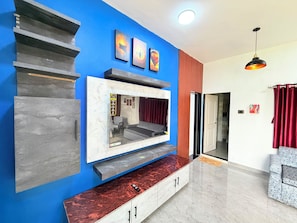 A modern living room with a blue accent wall, a built-in entertainment unit, and a red curtain. - Adiva Villa By Vintara Stays (Murud)
