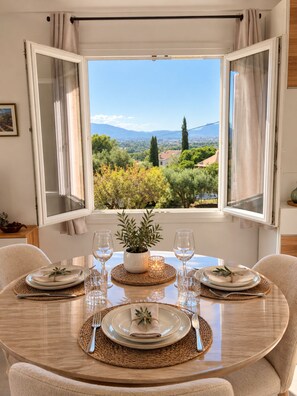 A dining table set for four with a view of a mountainous landscape through open windows. - Les Arbousiers Studio, Fréjus (Fréjus)