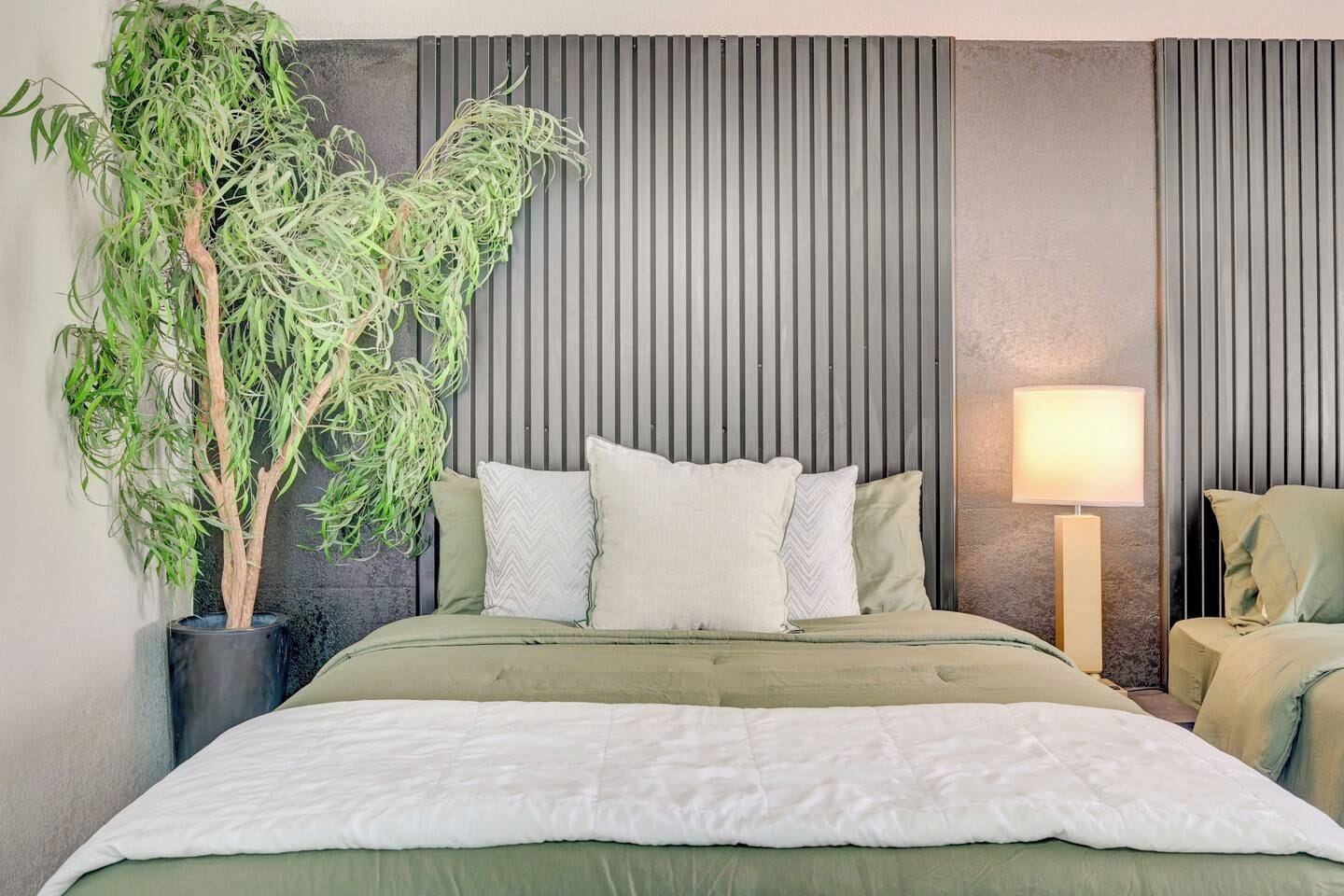 A modern bedroom with a bed, pillows, a bedside lamp, and a potted plant.