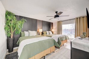 Ein Hotelzimmer mit zwei Betten, einem Deckenventilator, einem großen Fenster mit Vorhängen und einer Topfpflanze.