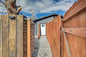 Ein schmaler Weg führt zu einem Haus mit der Hausnummer 211, einer Backsteinmauer und einem gemusterten Boden.