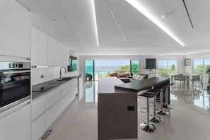 A modern kitchen with a central island, a dining area with a view of the ocean, and a living space with a large window overlooking the sea. - Penthouse w/ Ocean View, Oceania 331 by Bocobay (Noord)