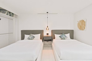 A hotel room with two beds, a ceiling fan, a bedside table with a lamp, and a wall with a leaf pattern. - Penthouse w/ Ocean View, Oceania 331 by Bocobay (Noord)