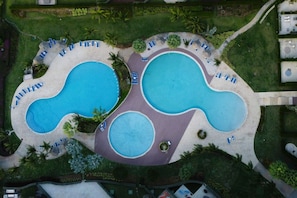 Eine Vogelperspektive zeigt ein Resort mit mehreren miteinander verbundenen Schwimmbecken, Liegebereichen und Wegen.
