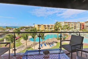 A balcony with a view of a swimming pool, lounge chairs, and a hotel building in the background. - Penthouse w/ Ocean View, Oceania 331 by Bocobay (Noord)
