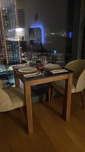 A dining area with a table set for two, a city view through a large window, and a modern interior design. - İzmir’in kalbinde ışık şölenine hazır mısınız? (İzmir)