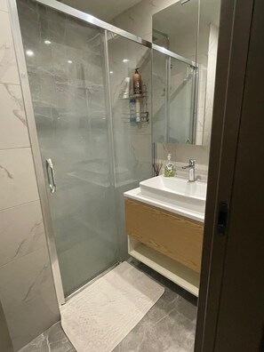Ein modernes Badezimmer mit Duschkabine aus Glas, einem weißen Waschbecken und einem Spiegel darüber.
