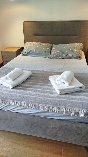 A neatly made bed with a grey blanket and two folded white towels. - İzmir’in kalbinde ışık şölenine hazır mısınız? (İzmir)