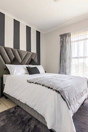 A modern bedroom with a bed, a headboard, and a window with curtains. - Beautiful View With Netflix and Fast Wifi (Johannesburg)