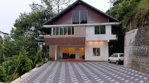 Een tweelaags huis met een balkon, een auto ervoor en een verharde oprit.