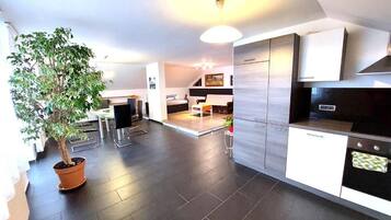 A modern kitchen with dark flooring, a potted plant, and a dining area with a table and chairs.