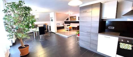 A modern kitchen with dark flooring, a potted plant, and a dining area with a table and chairs.