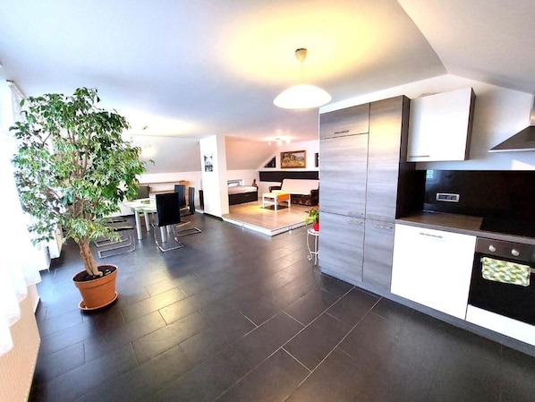 A modern kitchen with dark flooring, a potted plant, and a dining area with a table and chairs.