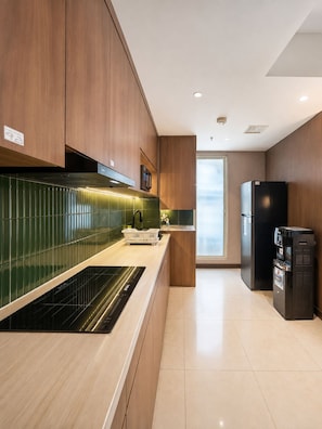 A modern kitchen with wooden cabinets, a black refrigerator, and a built-in oven. - Kisah By SanLiving - 3BR - Kasablanka (Jakarta)