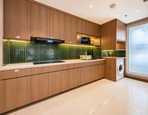 A modern kitchen with wooden cabinets, a microwave, and a built-in washing machine. - Kisah By SanLiving - 3BR - Kasablanka (Jakarta)