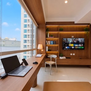 A modern office space with a desk, laptop, chair, and a television mounted on the wall displaying a movie. - Kisah By SanLiving - 3BR - Kasablanka (Jakarta)