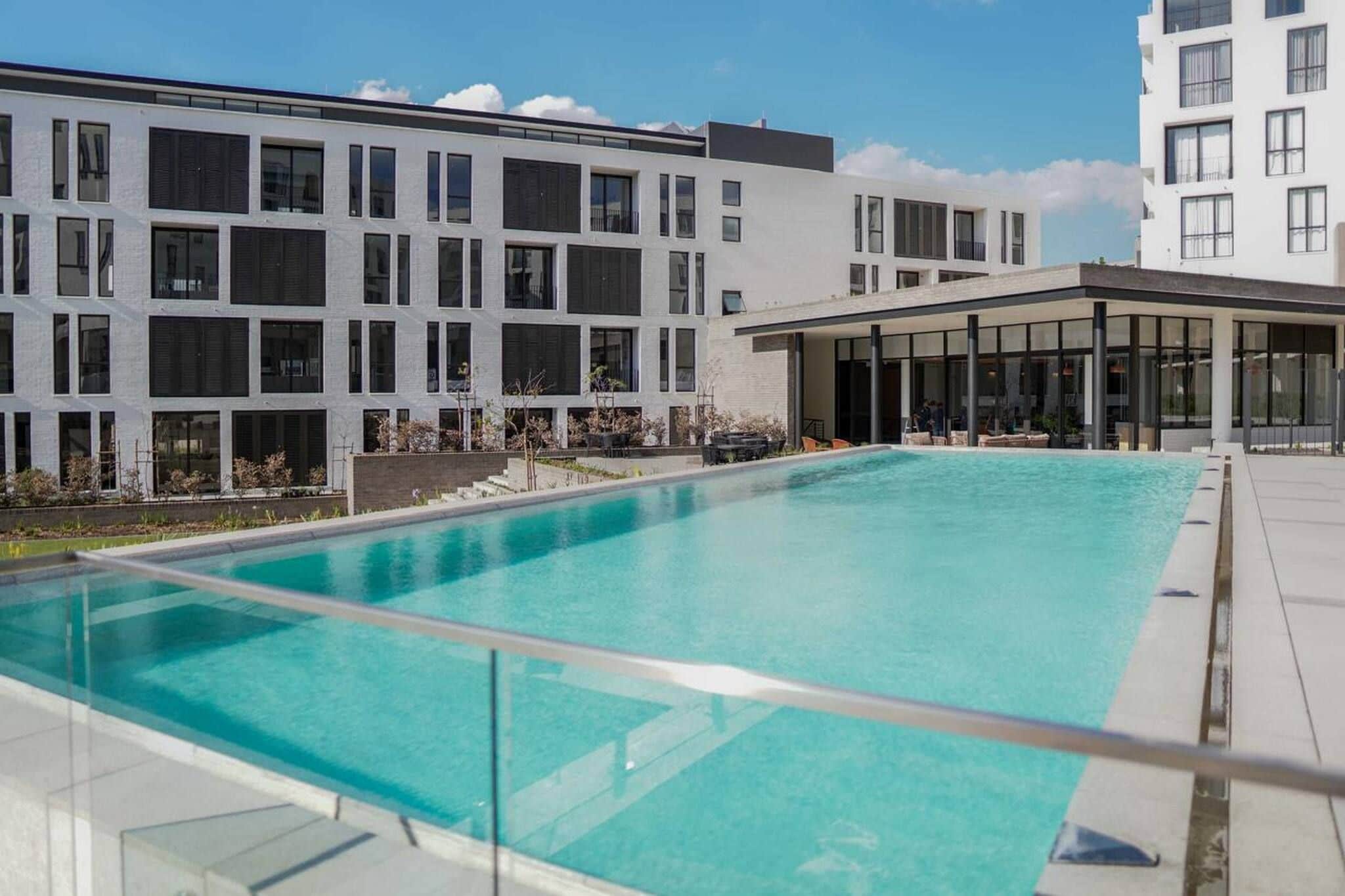 Um edifício moderno com piscina no terraço, grandes janelas e área externa coberta.