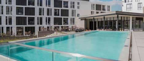 A modern building with a rooftop pool, large windows, and a covered outdoor area.