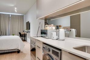 A modern hotel room with a bed, a desk, a flat-screen TV, a coffee machine, a kettle, and a built-in washing machine. - Rosebank Retreat, Business or Leisure (Johannesburg)