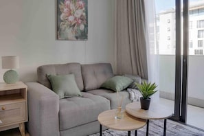 A modern living room with a sofa, two cushions, a side table with a lamp, a small round table with a plant, and a painting on the wall. - Rosebank Retreat, Business or Leisure (Johannesburg)