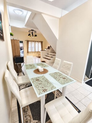 A dining area with a white table, cushioned chairs, a patterned table runner, and a ceiling light fixture. - Charming 2-bedroom House Rental in Muang Pattaya (Pattaya)