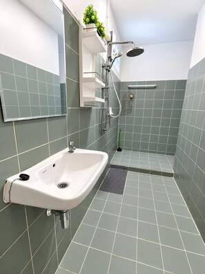 A modern bathroom with a white sink, a shower with a handheld showerhead, and a small shelf with a plant. - Charming 2-bedroom House Rental in Muang Pattaya (Pattaya)