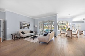 A spacious living room with a beige sofa, a coffee table, and a dining area with a table and chairs. - Spacious Naples Vacation Home | Sunshine & Relaxation (Lely Resort)