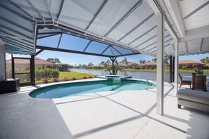 A covered outdoor swimming pool with a view of a lake and hills. - Spacious Naples Vacation Home | Sunshine & Relaxation (Lely Resort)