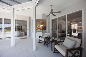 A covered patio with sliding glass doors, a ceiling fan, and outdoor furniture. - Spacious Naples Vacation Home | Sunshine & Relaxation (Lely Resort)