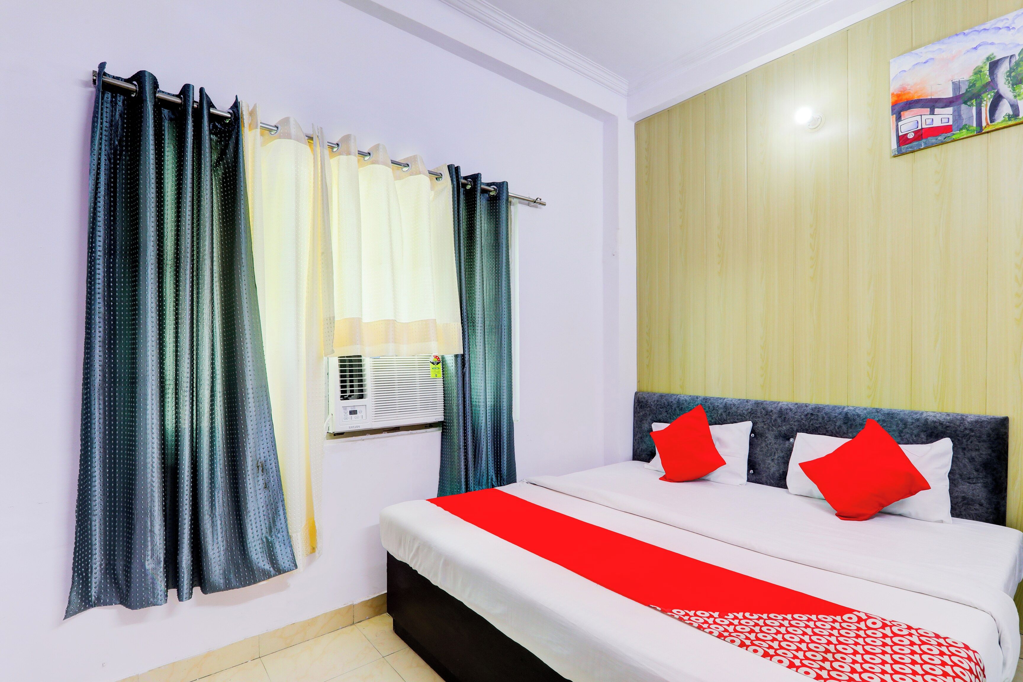 A hotel room with a bed, curtains, an air conditioning unit, and a wall-mounted artwork.
