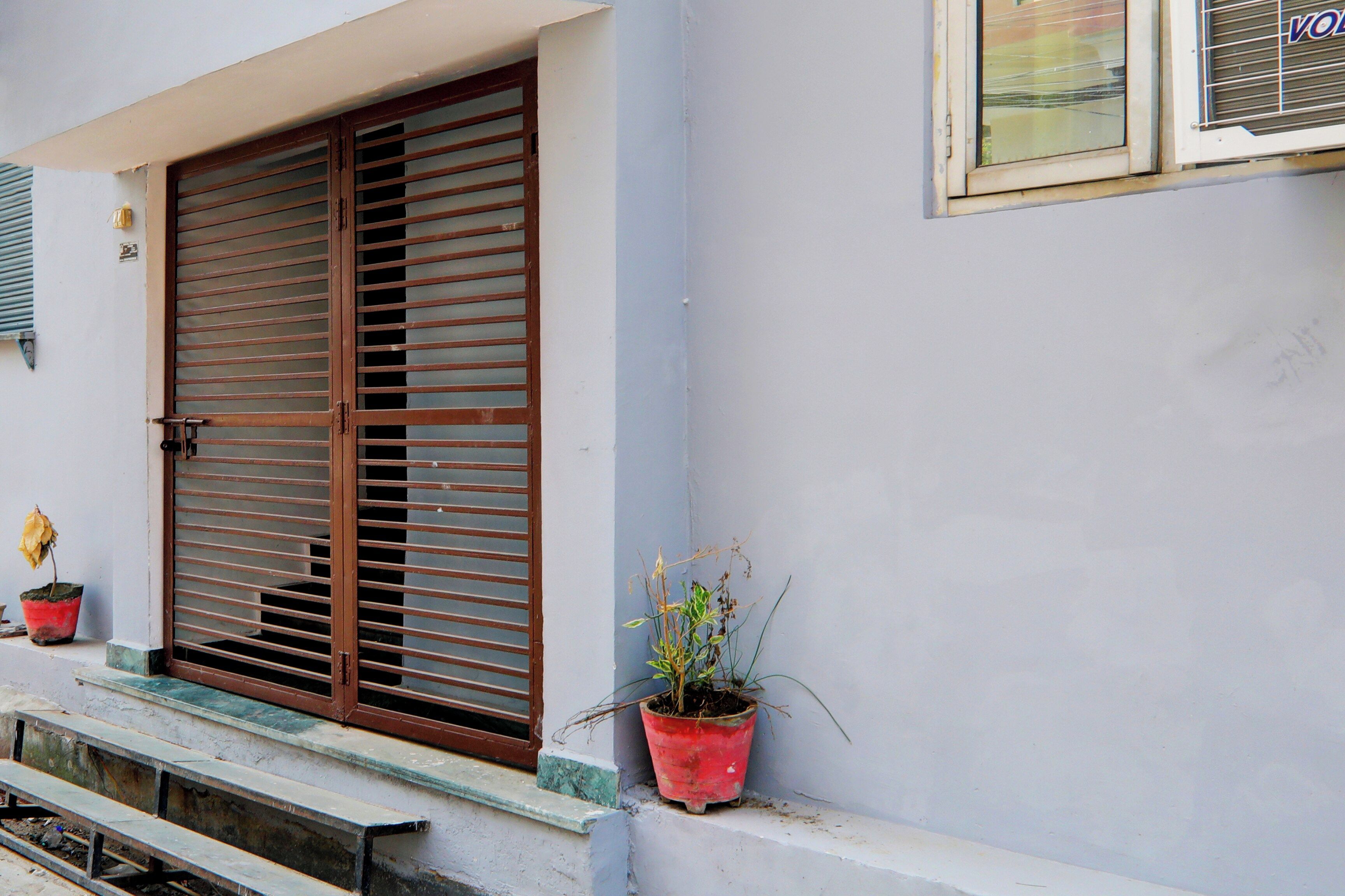 Un edificio con un gran ventanal con persianas horizontales, una pequeña planta en maceta en el alféizar y otra ventana con un nombre de marca visible.