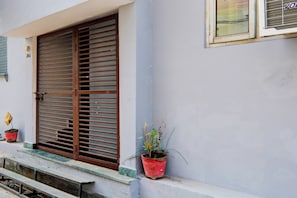 Un edificio con un gran ventanal con persianas horizontales, una pequeña planta en maceta en el alféizar y otra ventana con un nombre de marca visible.