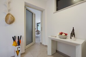 A hallway with a white console table, a decorative wall piece, and a door leading to a dining area. - Stunning villa with private pool in Taormina - DiCasaInSicilia (Taormina)