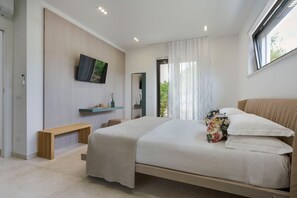 Une chambre à coucher moderne avec un grand lit, un téléviseur à écran plat fixé au mur, un banc en bois et une fenêtre ornée de rideaux légers.