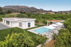 Uma casa moderna com piscina, cercada por vegetação e montanhas ao fundo.