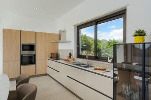 A modern kitchen with built-in appliances, a large window, and a dining area with a table and chairs. - Stunning villa with private pool in Taormina - DiCasaInSicilia (Taormina)