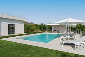 Uma área moderna com piscina ao ar livre, água azul cristalina, espreguiçadeiras brancas e um espaço coberto para relaxar.
