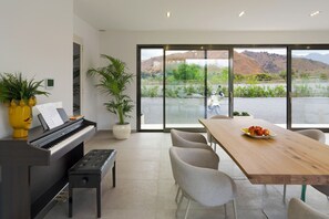 A modern interior with a piano, dining table, chairs, and a large window offering a view of a hilly landscape. - Stunning villa with private pool in Taormina - DiCasaInSicilia (Taormina)
