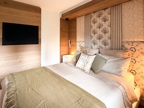 A bedroom with a bed, pillows, a bedside table, and a wall-mounted TV. - Chalet Larice: wood-clad mountain home with balcony, sleeps 4/max6, Sauze d'Oulx (Sauze d'Oulx)