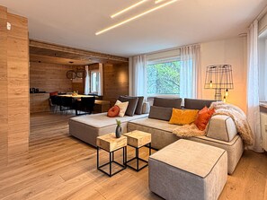 A modern living room with a sofa, ottoman, and coffee table, wooden flooring, and a dining area with a table and chairs. - Chalet Larice: wood-clad mountain home with balcony, sleeps 4/max6, Sauze d'Oulx (Sauze d'Oulx)