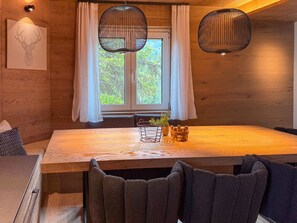 A dining area with a wooden table, dark upholstered chairs, a potted plant, and a wall-mounted light fixture. - Chalet Larice: wood-clad mountain home with balcony, sleeps 4/max6, Sauze d'Oulx (Sauze d'Oulx)