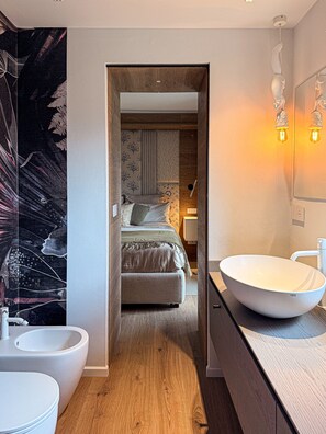 A modern bathroom with a large white basin, a wooden floor, and a bed with patterned bedding in the background. - Chalet Larice: wood-clad mountain home with balcony, sleeps 4/max6, Sauze d'Oulx (Sauze d'Oulx)